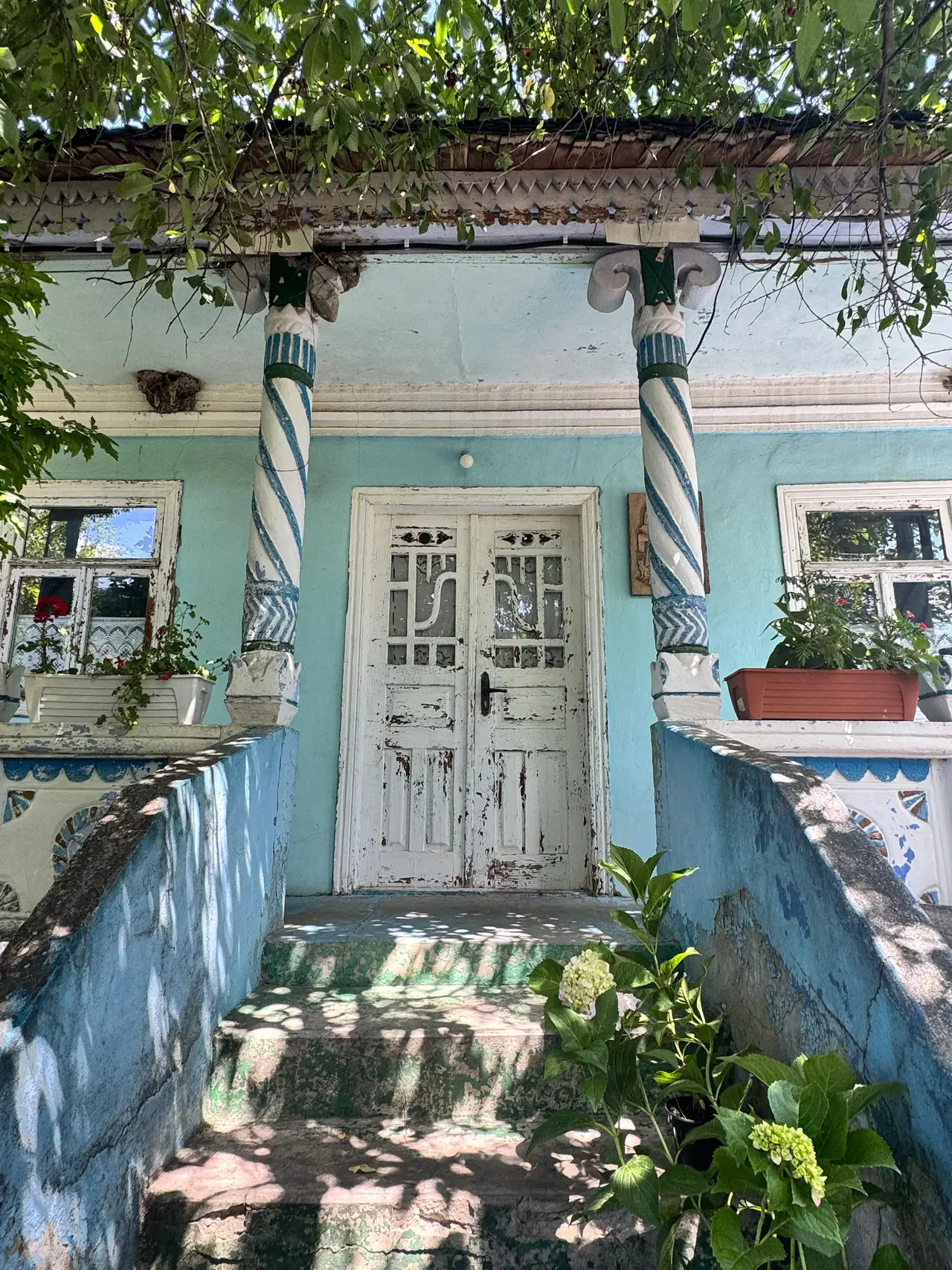 Traditional Moldovan house with turquoise walls, white wooden doors and decorative spiral columns with hanging willow branches