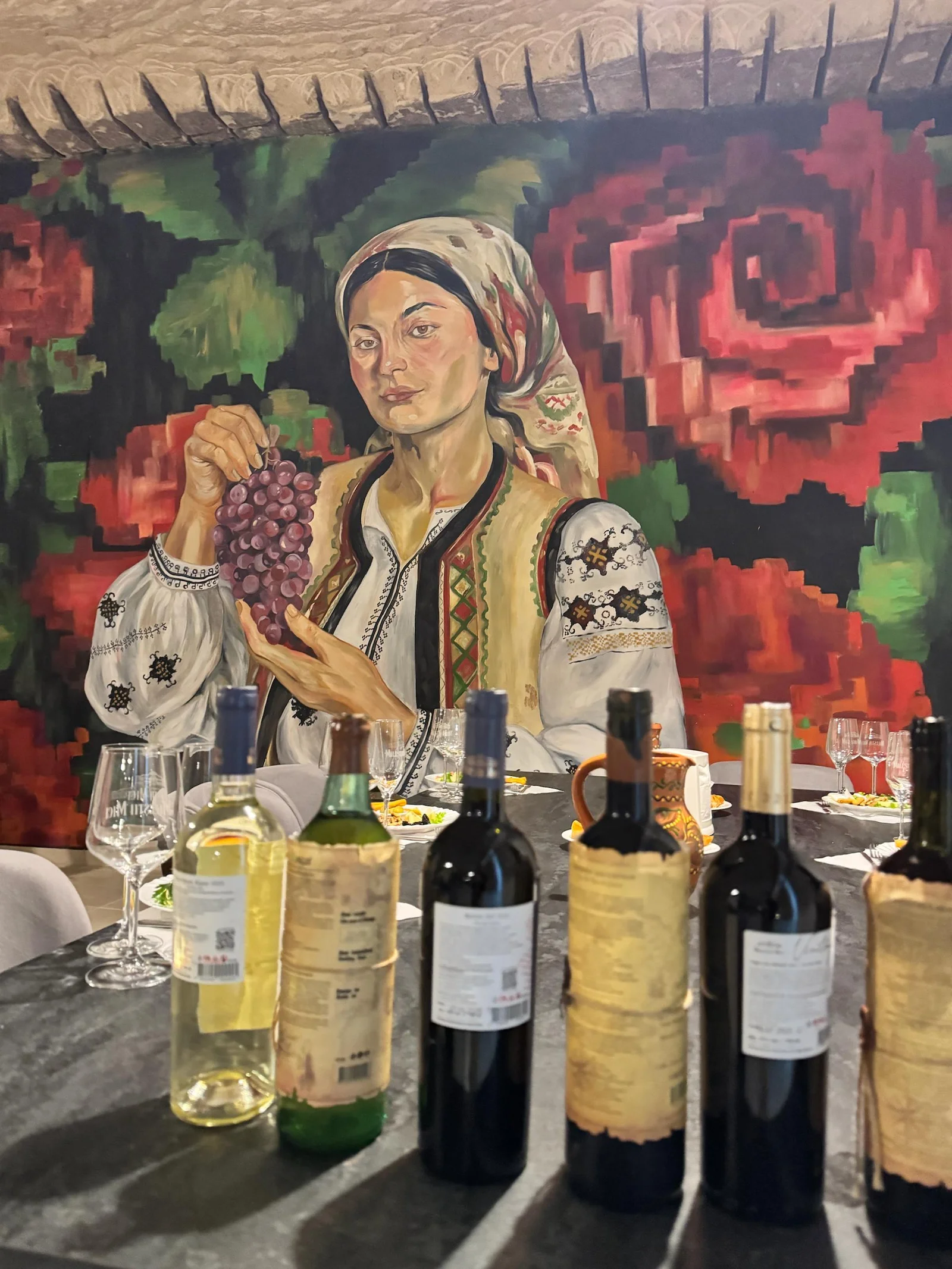 Wine tasting setup with bottles displayed in front of a mural featuring a woman in traditional Moldovan clothing holding grapes